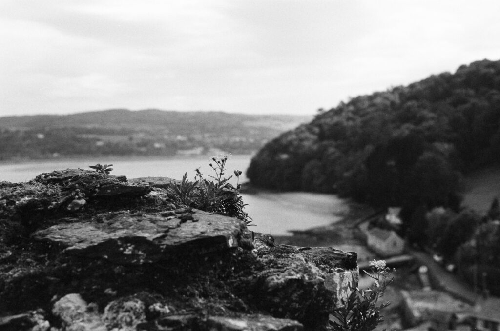 Black and white view from a rocky ledge overlooking a river and hills.
