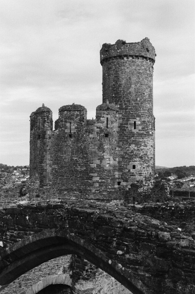 A black-and-white view of a stone castle tower with a high, cylindrical turret rising above ruined walls.