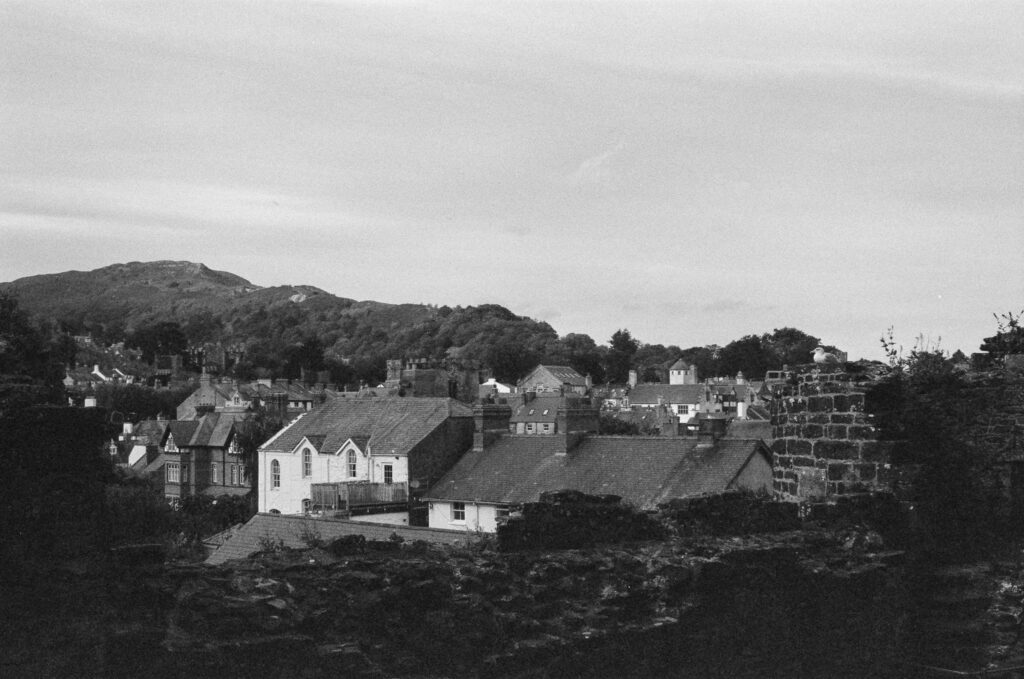 A view of a small town with houses and stone buildings nestled beneath a forested hill.