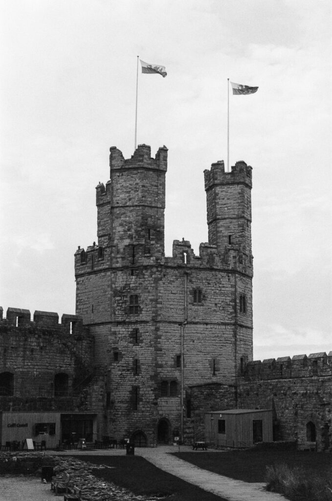 The tall stone towers of Caernarfon Castle with two flags flying from the battlements.