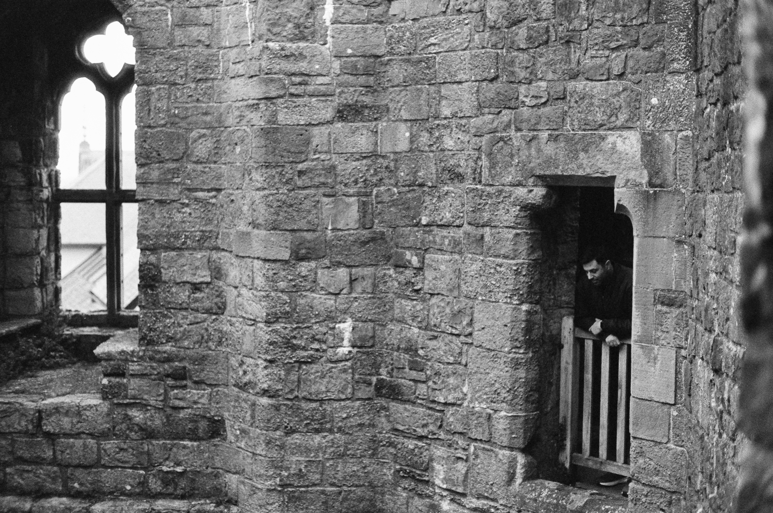 A person stands in a stone doorway of a castle ruin, looking out over a wooden railing.
