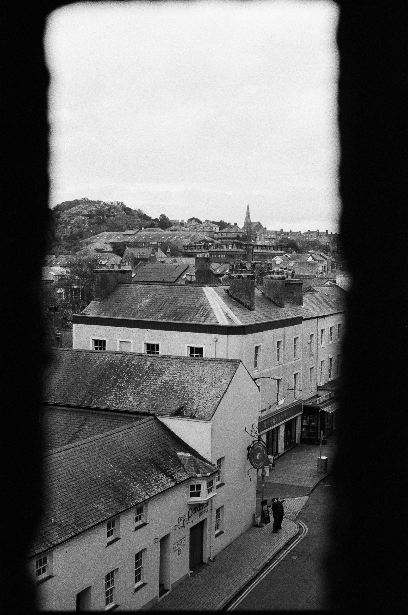 A black and white view of a town street and buildings framed by a dark, vertical window or doorway.