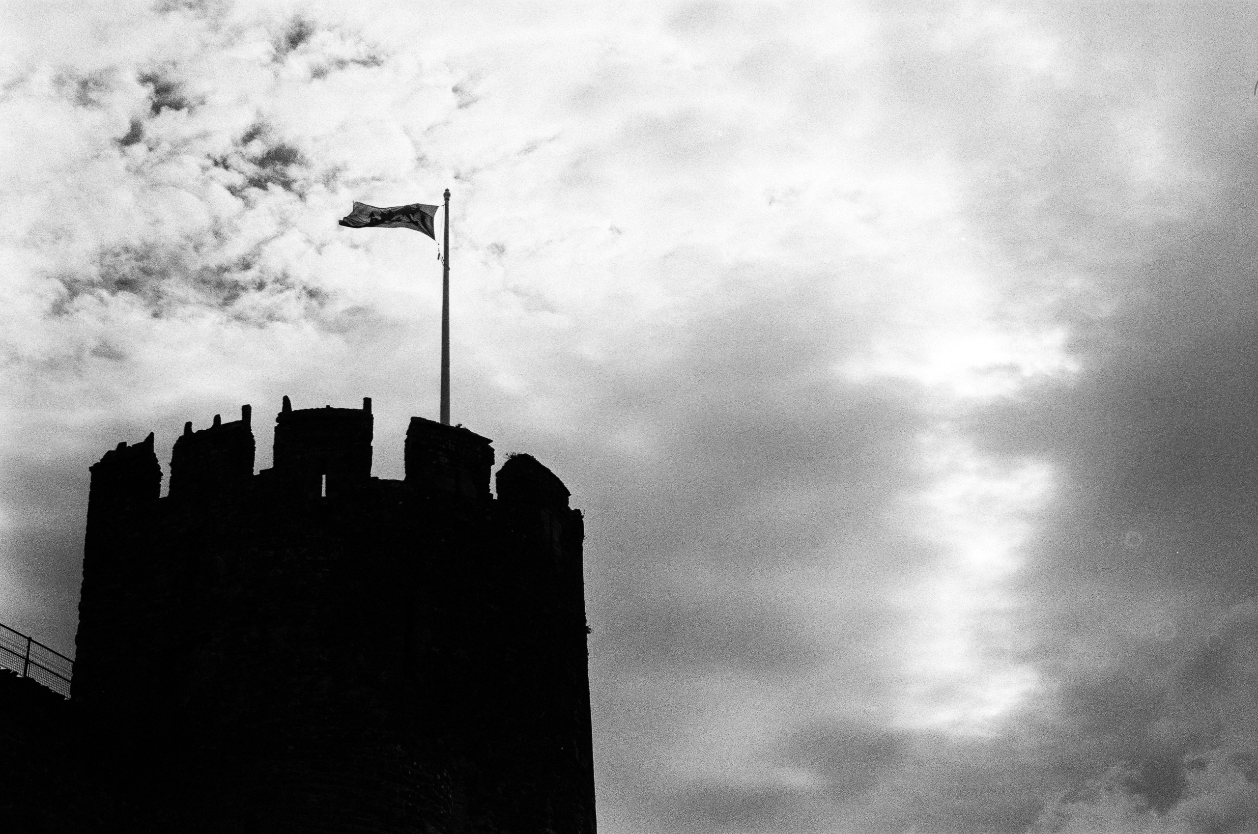 A silhouette of a castle turret against a cloudy sky with a flag flying from a flagpole.