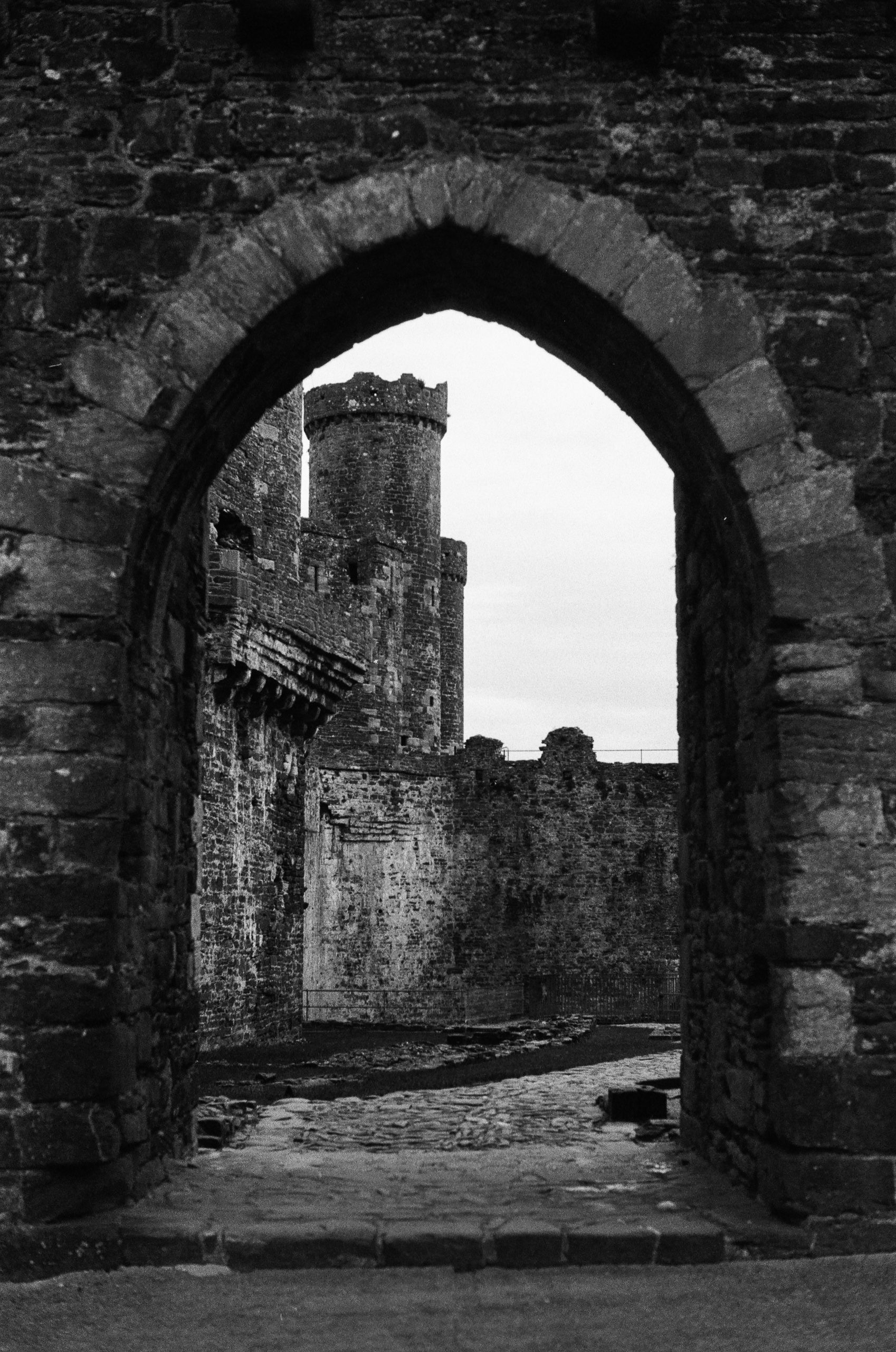 View through a stone archway of a castle courtyard with a tall tower and defensive walls.