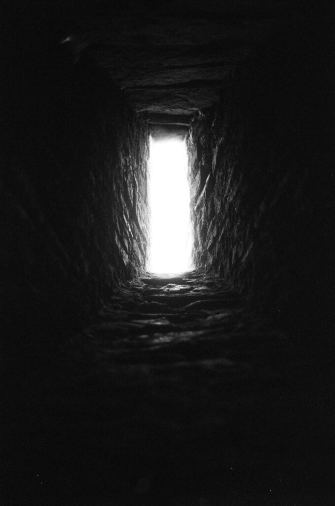 Bright light shines through a narrow, dark stone slit.