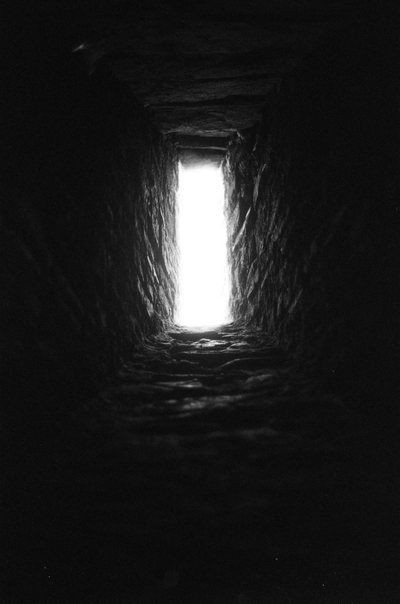 Bright light shines through a narrow, dark stone slit.