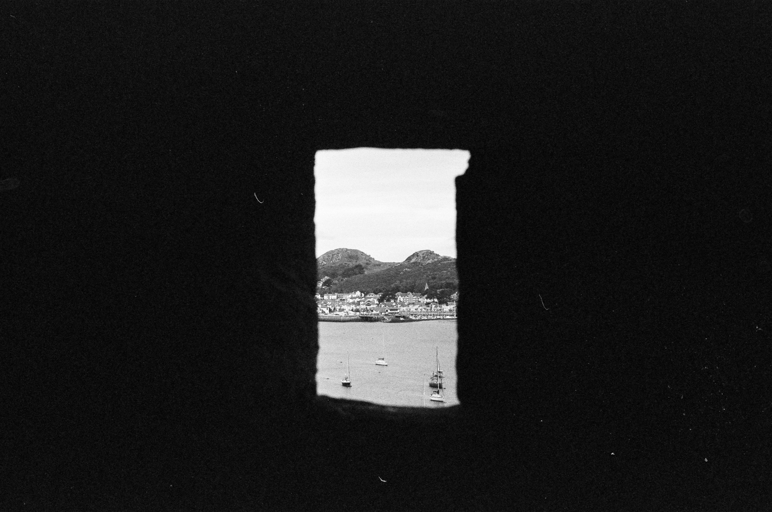 A rectangular view of a coastal town, harbor, and hills framed by a dark, stone opening.